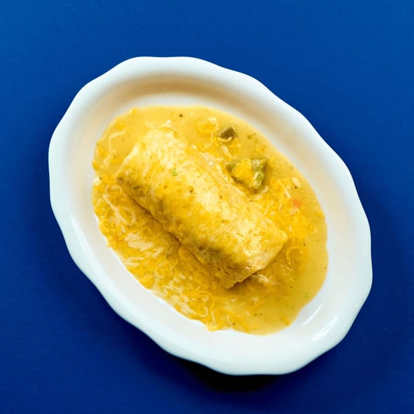 A large, golden-brown burrito covered in a creamy yellow sauce and shredded cheese on a white plate.