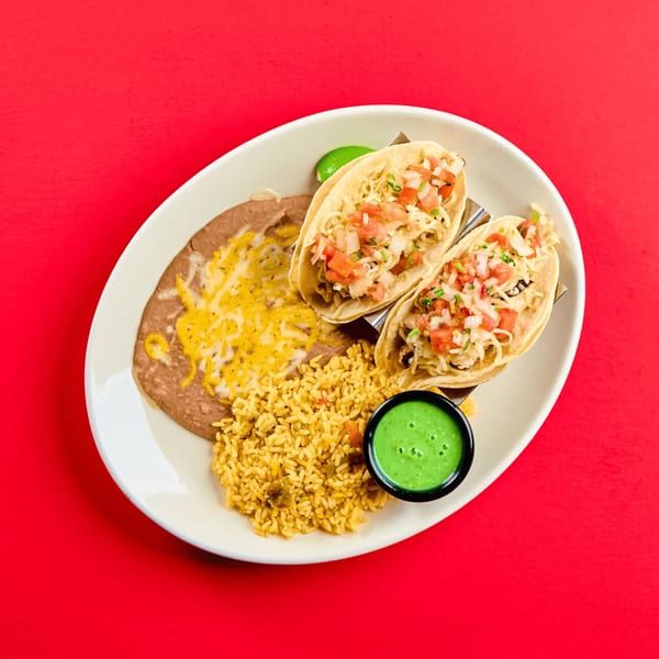 Two La Bamba chicken tacos with rice, refried beans, and green sauce on a white plate.