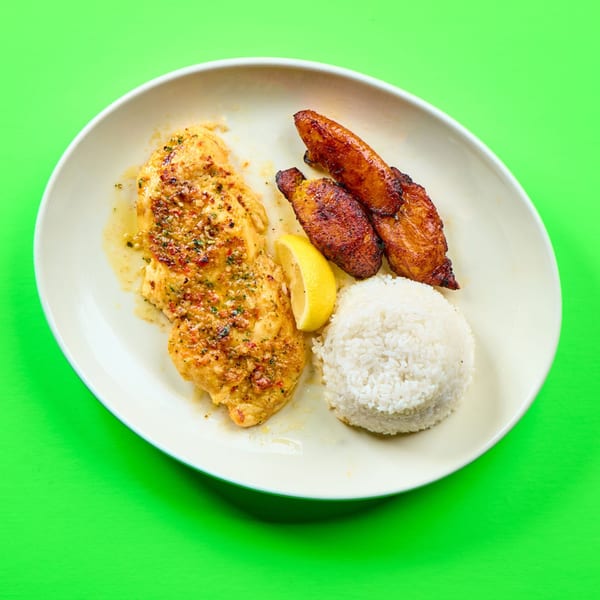 La Bamba's chicken dish with rice, fried plantains, and a lemon wedge on a white plate.