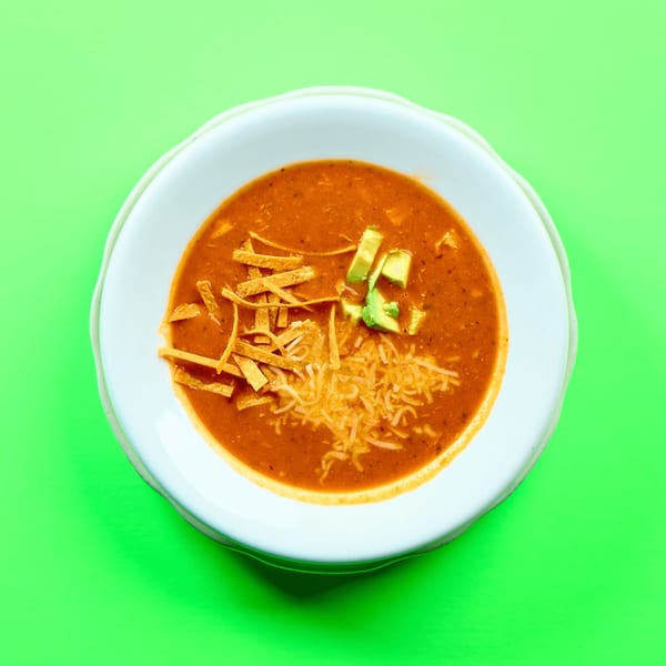La Bamba's tortilla soup, garnished with tortilla strips, shredded cheese, and avocado, on a green background.