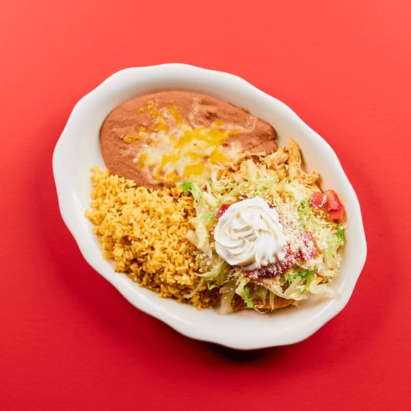 A La Bamba Mexican dish with refried beans, rice, shredded chicken, lettuce, tomatoes, and sour cream.