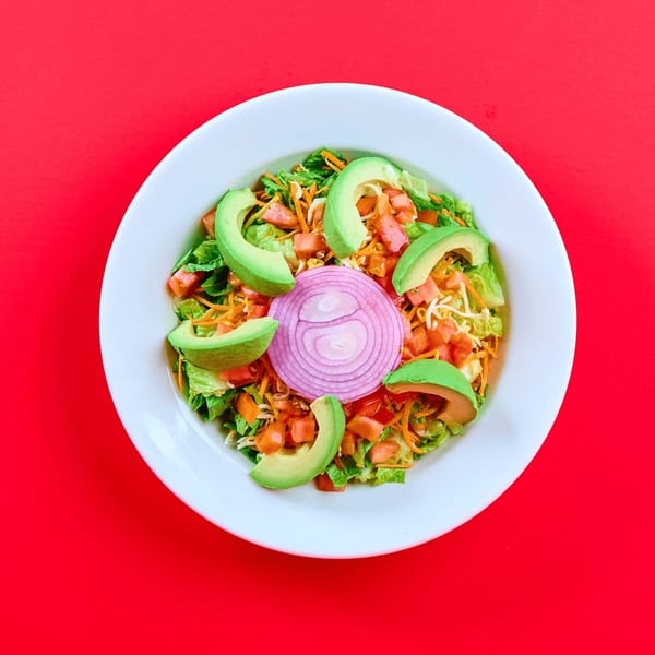 A vibrant Mexican salad with lettuce, tomatoes, avocado slices, shredded cheese, and red onion.